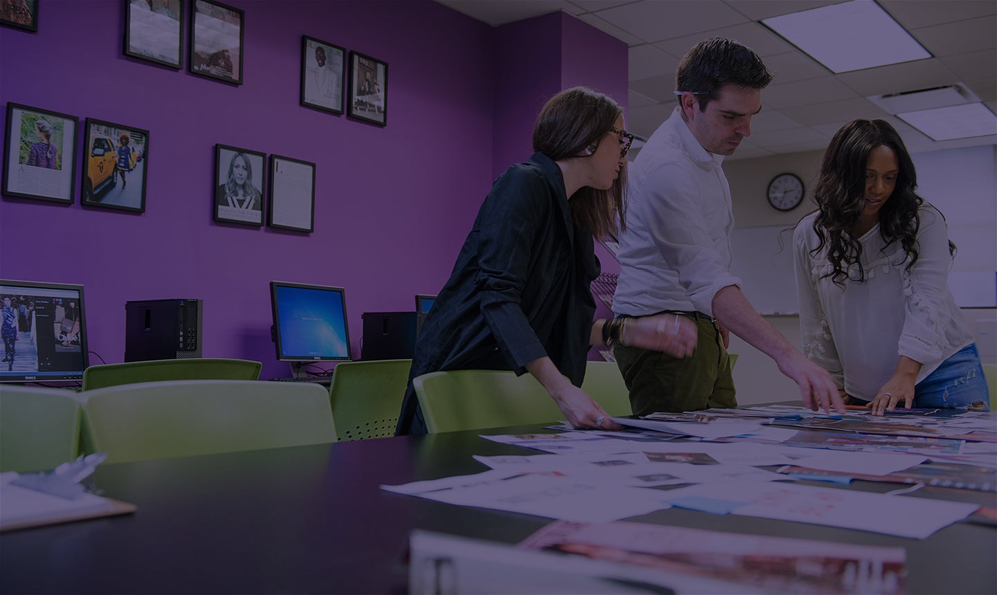 Three people working over a table of designed papers.