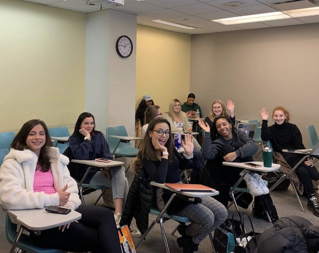 Students in a classroom waving at the camera