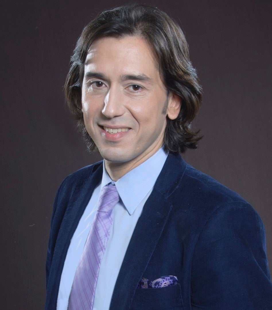 A headshot of LIM professor Burak Ayata, wearing a blue shirt with purple tie