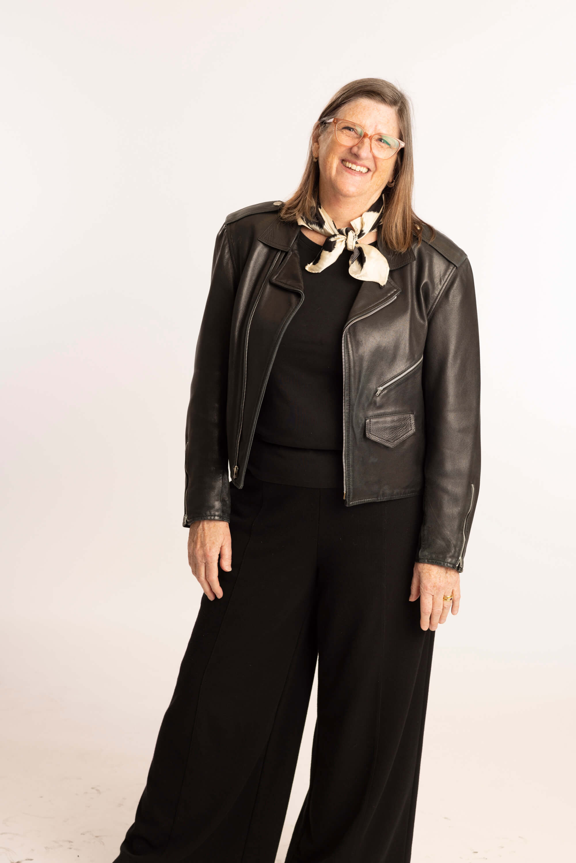 A photo of LIM professor Patty Mitropoulos, who wears a black leather jacket, and a black and white scarf tied around her neck
