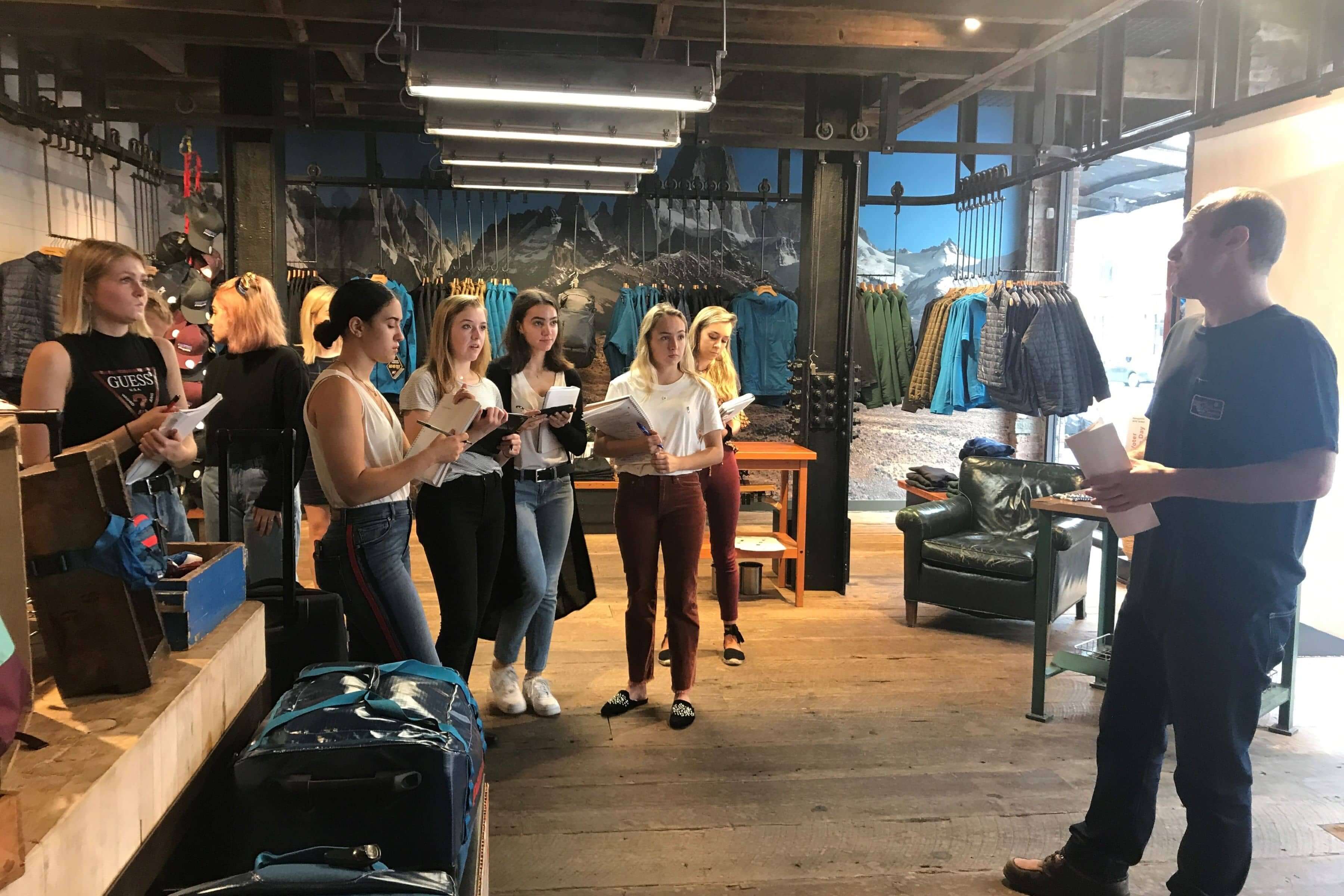 LIM students visit a Patagonia store. They take notes on notepads while a store employee gives a talk