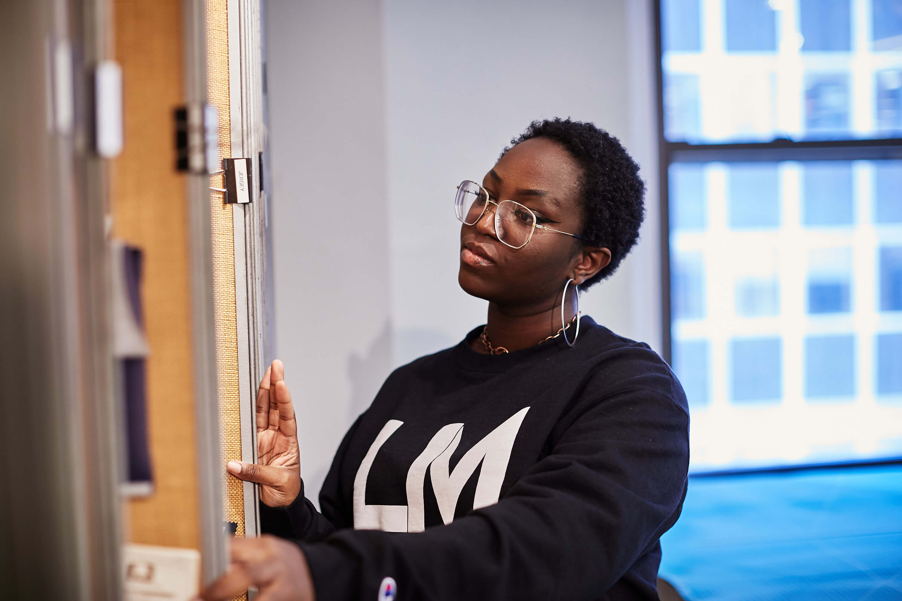 Female student in a black-and-white LIM sweatshirt looks at panels containing fabric swatches