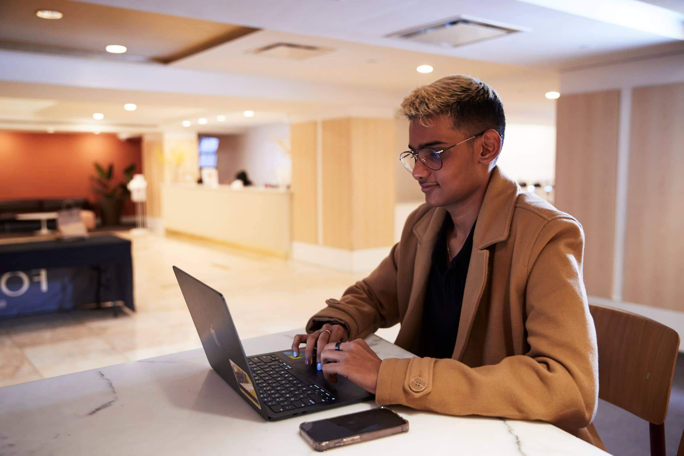 A LIM student types on a laptop whie sitting in the lobby of FOUND Study residential hall building in New York City