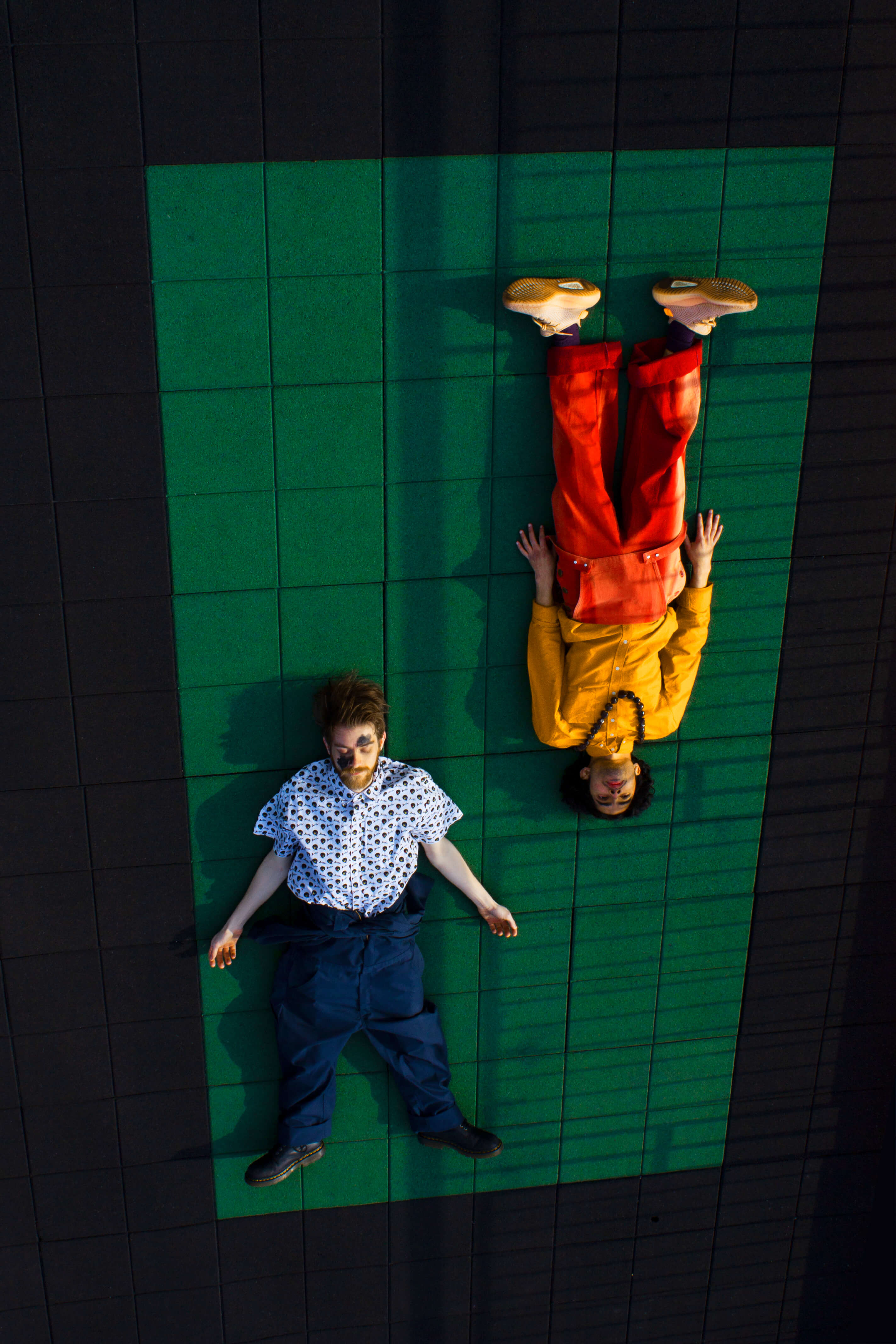 photo from above of two people laying on a green floor