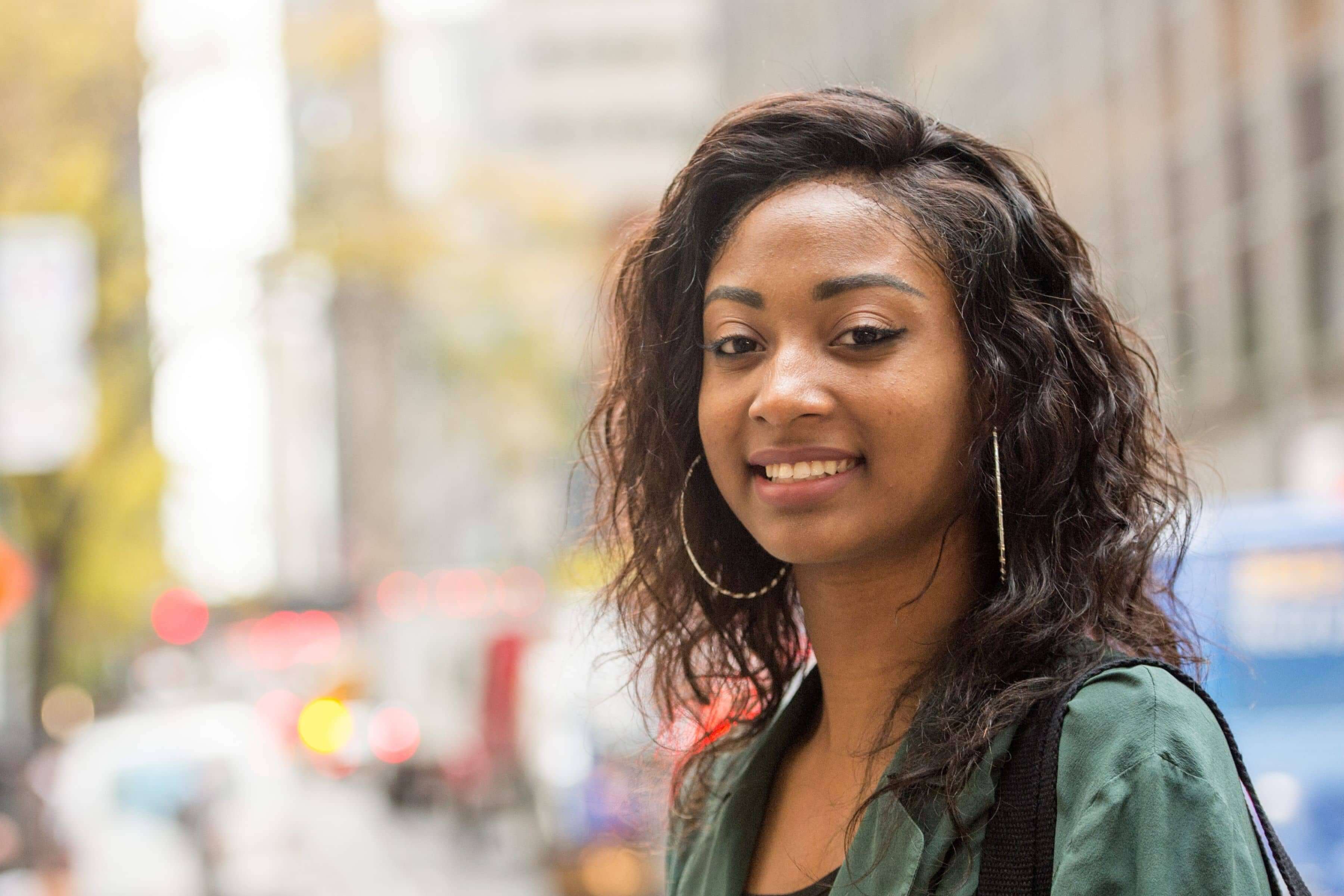 An LIM student with a green shirt and large hoop earrings poses in the streets of New York City