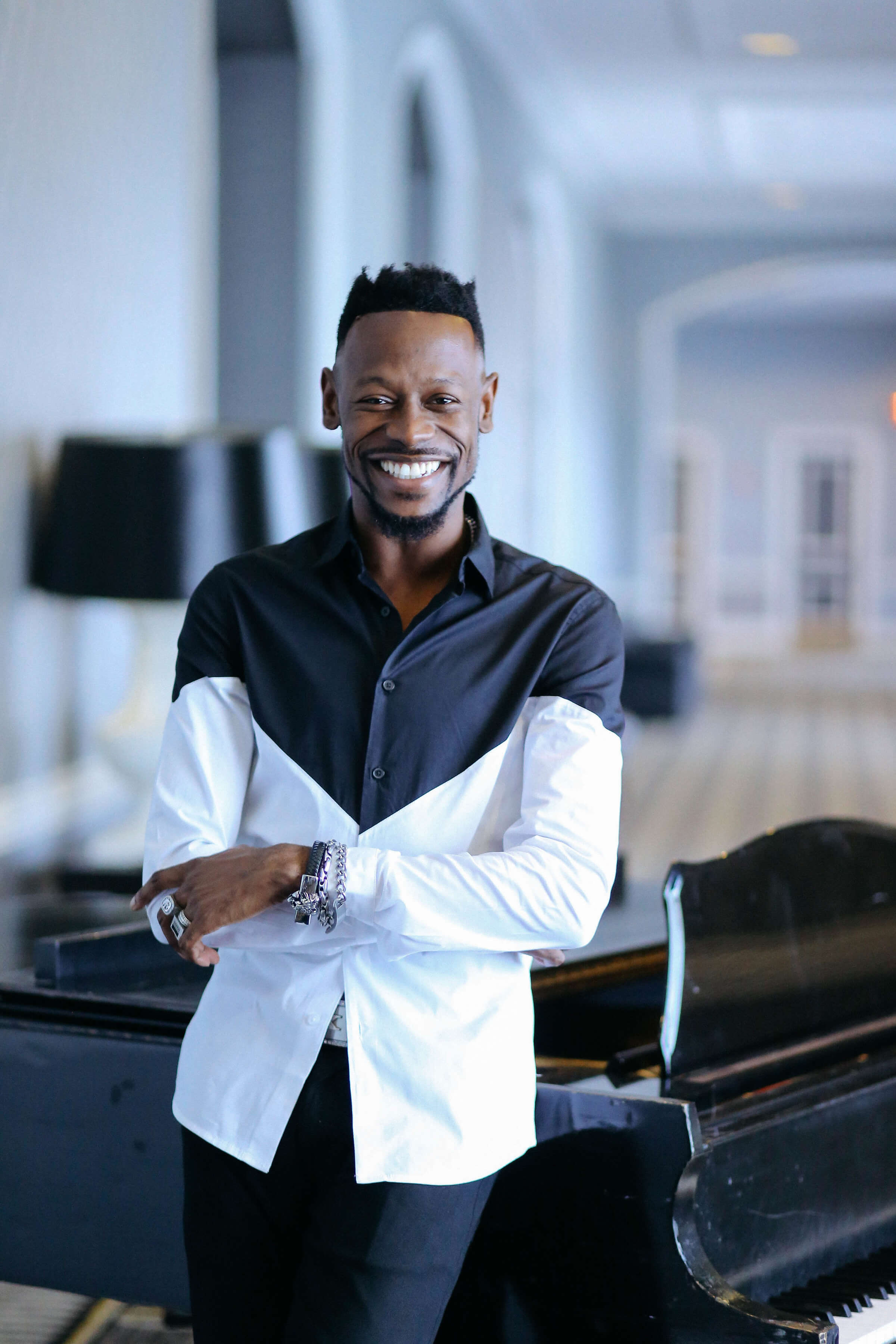 Man in a black and white shirt standing in front of a piano