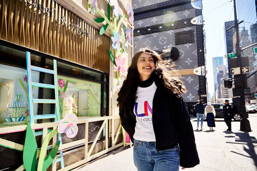 young woman, long dark hair, LIM shirt, walks near Fifth Avenue in NYC.