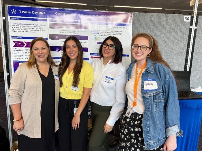 group of women, business casual attire, stand in front of a presentation screen smiling
