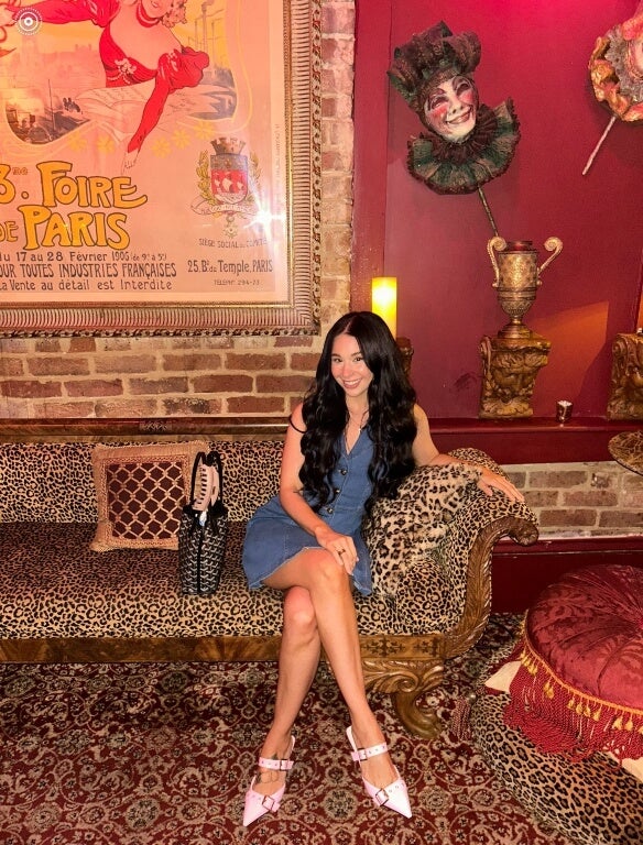young woman, long dark hair, sits on leopard-print couch in an ornate room, wearing a blue dress