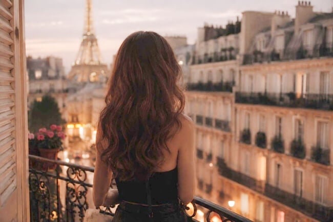 young woman shown from behind, long hair, standing on Parisian balcony