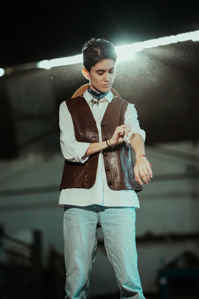 model with tight, dark hair in leather vest, jeans