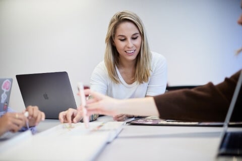 Blonde woman, white t-shirt, LIM College classroom setting with laptops.