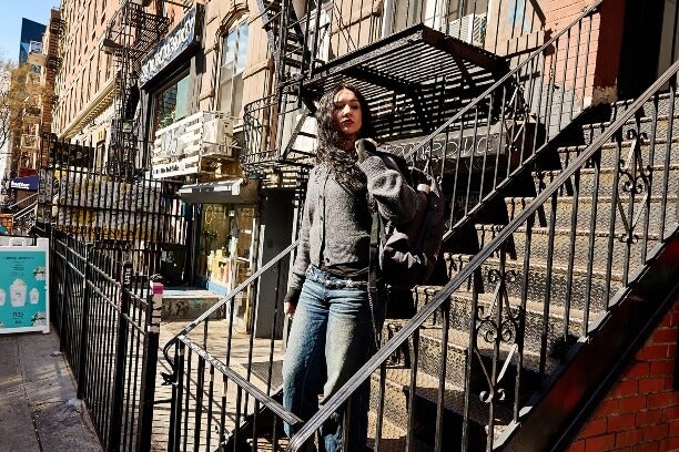 young woman, black hair, descends walkup building staircase to street level in New York City