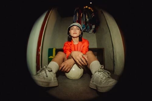 stylized fish-eye lens photo of a woman sitting with a soccer ball