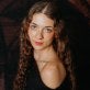young woman, long blonde curly hair headshot, dark sweapter off-the-shoulder