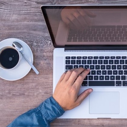 a left hand touching a laptop next to acoffee cup