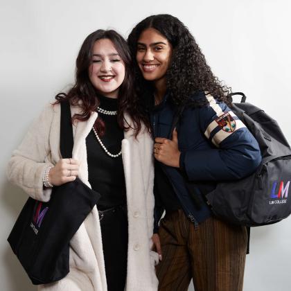 Two students in front of a white background with LIM bags