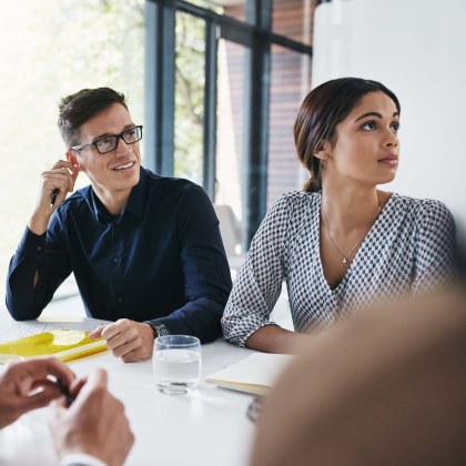 Individuals in business attire sit in a meeting room at a table