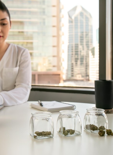 Woman at laptop with jars of cannabis on the desk.