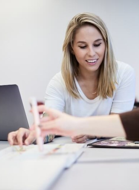 blonde female student, white t-shirt, in open concept classroom with laptop