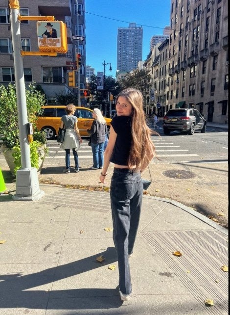 young woman, long brown hair, jeans, dark shirt, New York City street corner