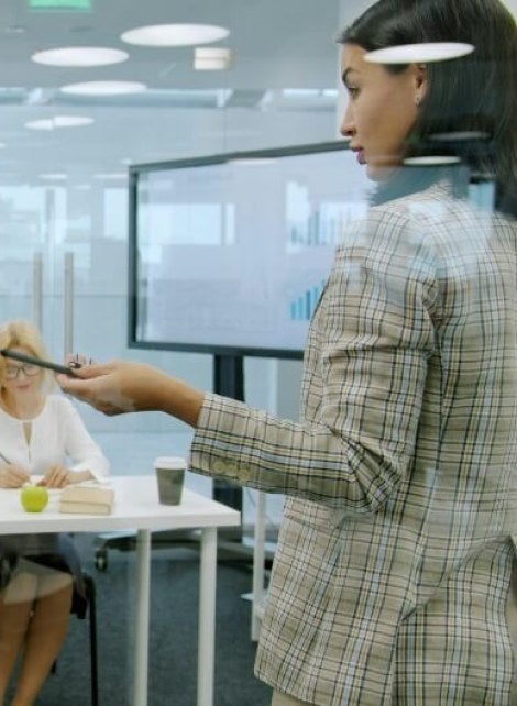young woman, brown hair, patterned jacket, presents in a meeting room in a corporate setting.