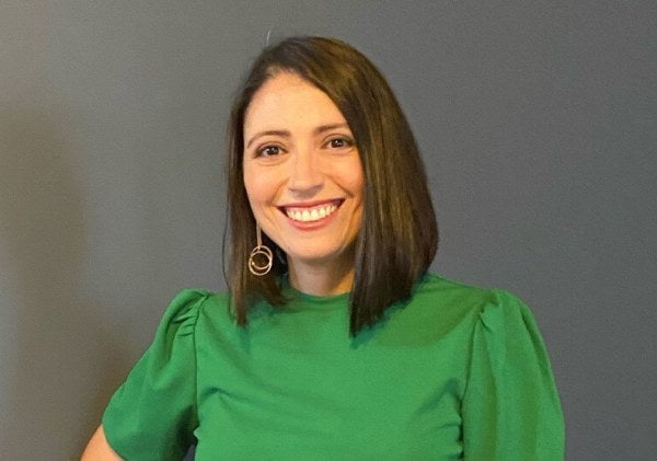 LIM alum Anna Bennudriti wears a green shirt against and smiles.