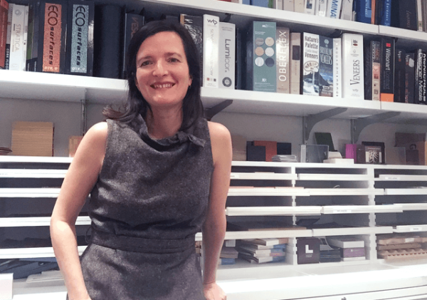 LIM professor Leonora Loeb wear a grey dress and stands in front of bookshelves