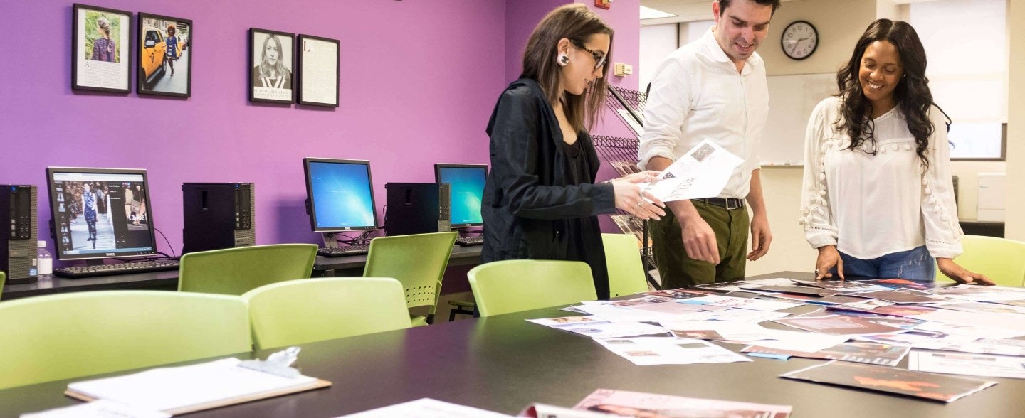 Three students look at magazine spreads on a table
