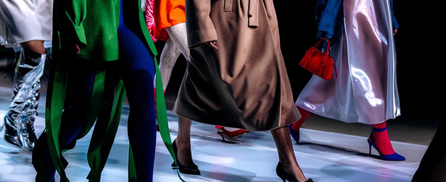 Models from neck down on runway, multicolored clothes and accessories