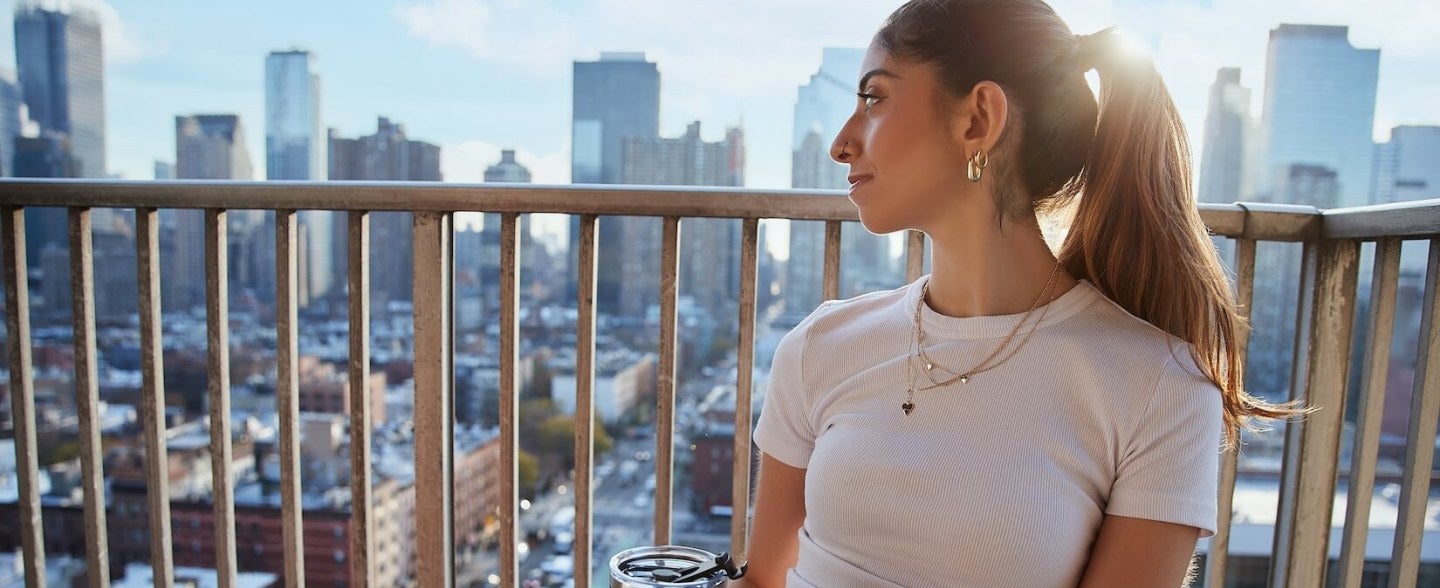 young woman, light-brown hair, beverage, balcony overlooking NYC