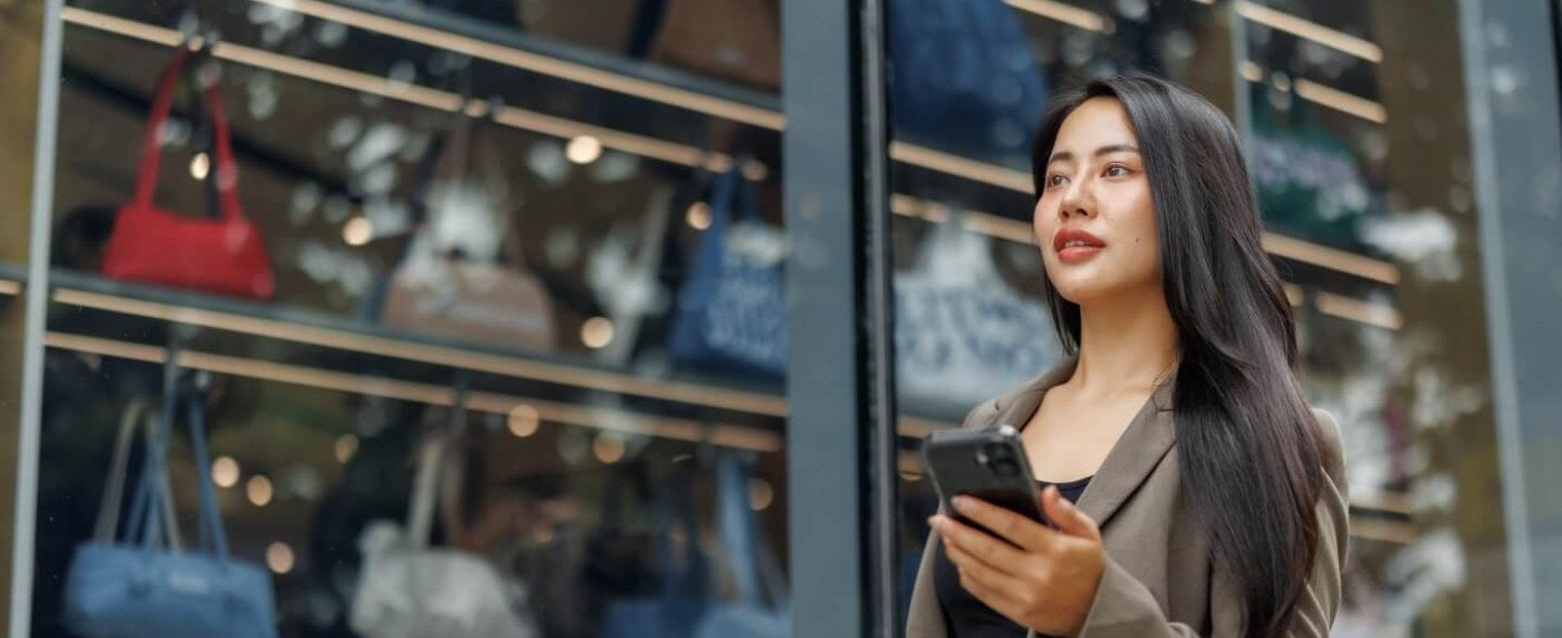woman on mobile device walking in front of handbag storefront window