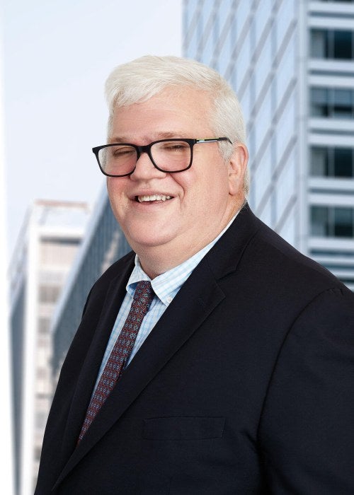 man in black suite with tie and glasses smiling at camera