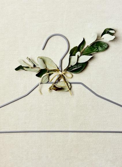 thin gray clothing hanger with leaves attached to it on beige background