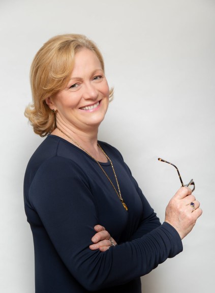 A woman standing sideways holding her glasses