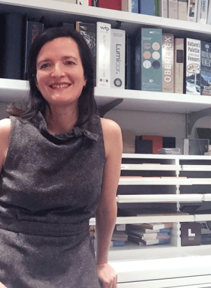 LIM professor Leonora Loeb wear a grey dress and stands in front of bookshelves