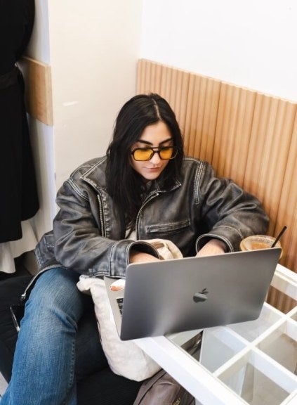 young woman, long dark hair, sunglasses, leather jacket, apple laptop, iced coffee