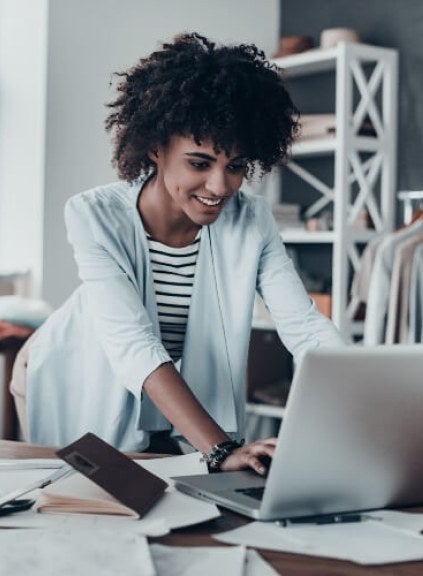 woman, curly black hair, white sweater, working on laptop in fashion company office