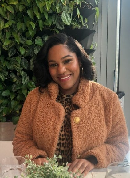 seated woman, shoulder-length dark hair, pink coat, foliage in background