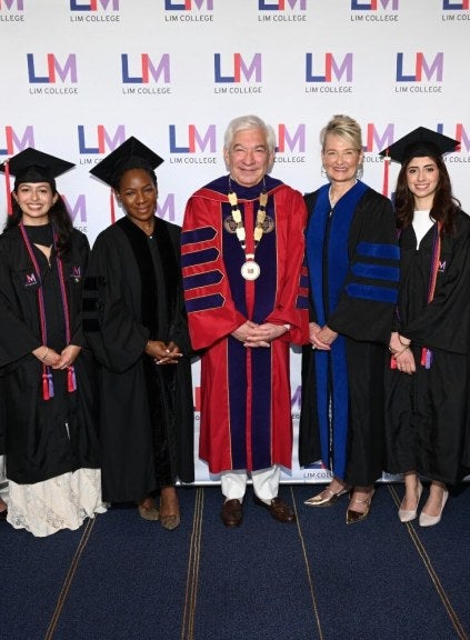 2026 LIM College Commencement step and repeat, Andrea, Tamika, Ron, Elyce, and Fernanda wearing academic graduation regalia 