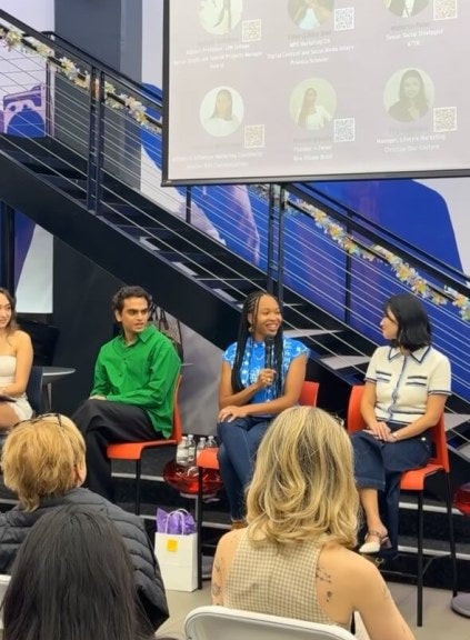 Several LIM College alumni sit on a panel in Maxwell Hall's student center. One of them holds a microphone.
