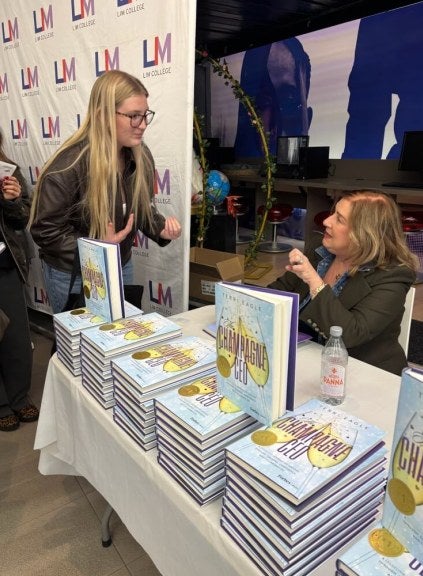 book-signing event, LIM College step-and-repeat in background, student with glasses and long blonde hair talks with author Terri Eagle