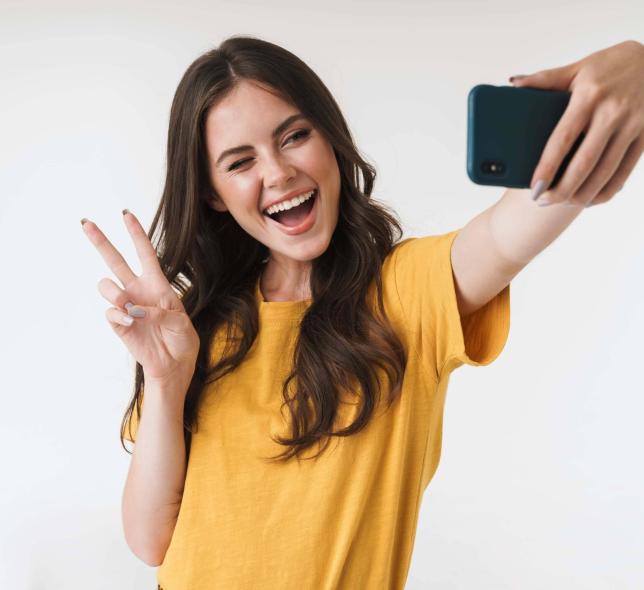 A woman makes a peace sign while taking a selfie