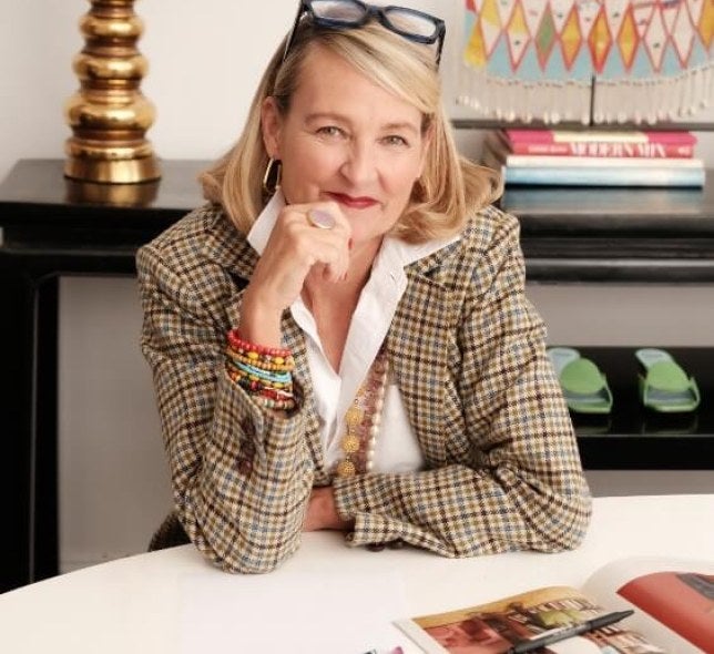 Blonde woman, checkered jacket, glasses, sits at desk with fashion patterns