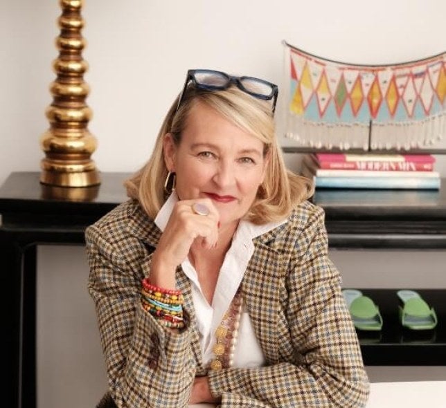 Blonde woman, checkered jacket, glasses, sits at desk with fashion patterns