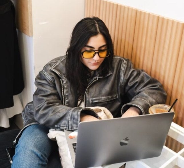 young woman, long dark hair, sunglasses, leather jacket, apple laptop, iced coffee