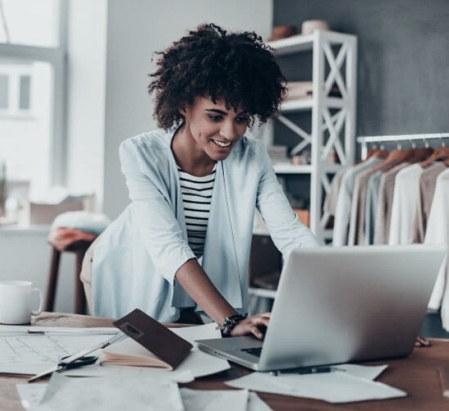 woman, curly black hair, white sweater, working on laptop in fashion company office