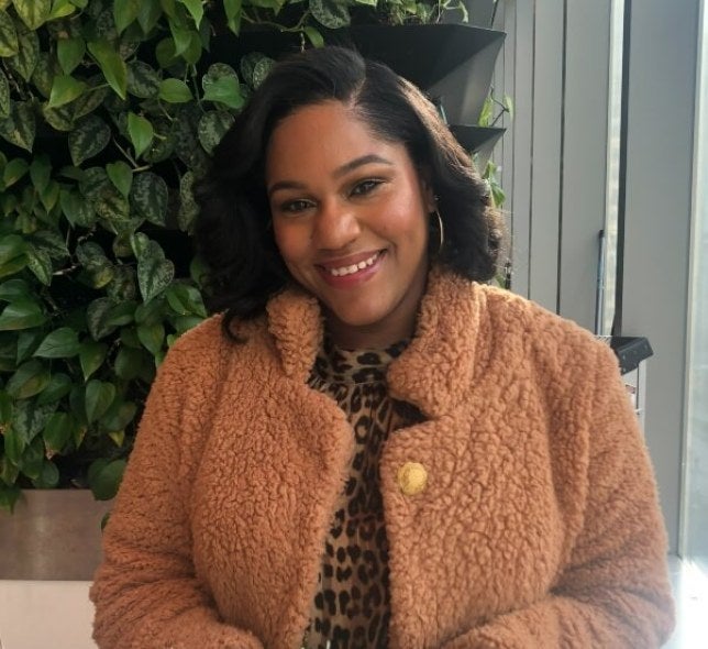 seated woman, shoulder-length dark hair, pink coat, foliage in background