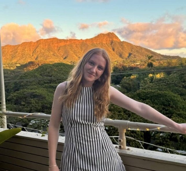 young woman, long red hair, outdoor balcony, mountains in background, vertical-striped dress
