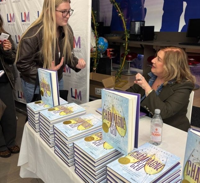 book-signing event, LIM College step-and-repeat in background, student with glasses and long blonde hair talks with author Terri Eagle